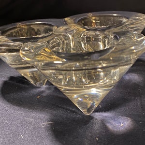 May include: A clear glass candle holder with three individual candle cups. The holder is shaped like a three-pointed star and has a unique, textured design.