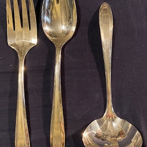 May include: A set of three silver-plated serving utensils, including a fork, a spoon, and a ladle. The utensils have a classic design with ornate handles.