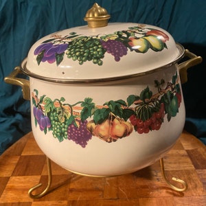 May include: White enamel pot with a gold trim and a fruit design. The pot has a lid with a gold knob and sits on a gold metal stand.