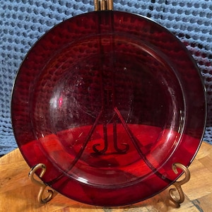 Può includere: Un piatto da portata in vetro rosso scuro con una superficie leggermente ondulata. Il piatto è su una superficie di legno.