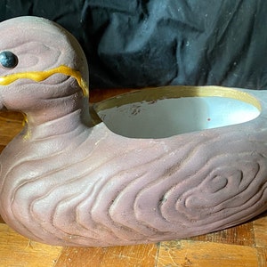 May include: A brown ceramic duck planter with a gold painted design. The planter has a white glazed interior and is perfect for small plants.