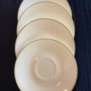 May include: Four white ceramic saucers with a green rim. The saucers are stacked on top of each other.
