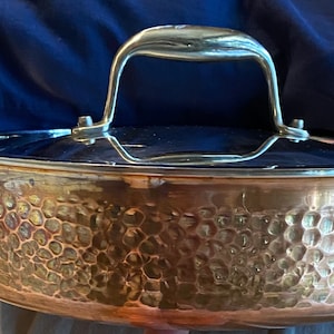 以下が含まれることがあります： 銀色の取っ手が付いた、ハンマーで叩いた銅製の鍋。鍋は、ハンマーで叩いたテクスチャ加工が施されており、幅広で丸い底をしています。