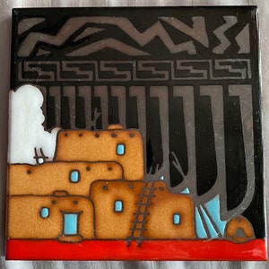 May include: A ceramic tile with a black background and a colorful depiction of a pueblo-style building with a ladder leading up to the roof. The building is painted in shades of brown, orange, and blue, with white accents. The background features a black and white geometric pattern.