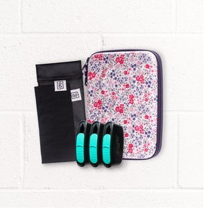 Könnte beinhalten: Eine Sammlung von Accessoires, darunter ein Etui mit floralem Muster, schwarze Beutel mit weißen Etiketten und drei schwarze und türkisfarbene Geräte. Das Etui hat einen Reißverschluss und ein Muster aus roten und blauen Blumen.