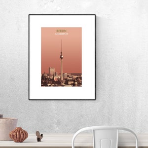 May include: A framed print of a cityscape with a tall tower in the center. The print is titled "Berlin Alexanderplatz" and has a red-orange background.