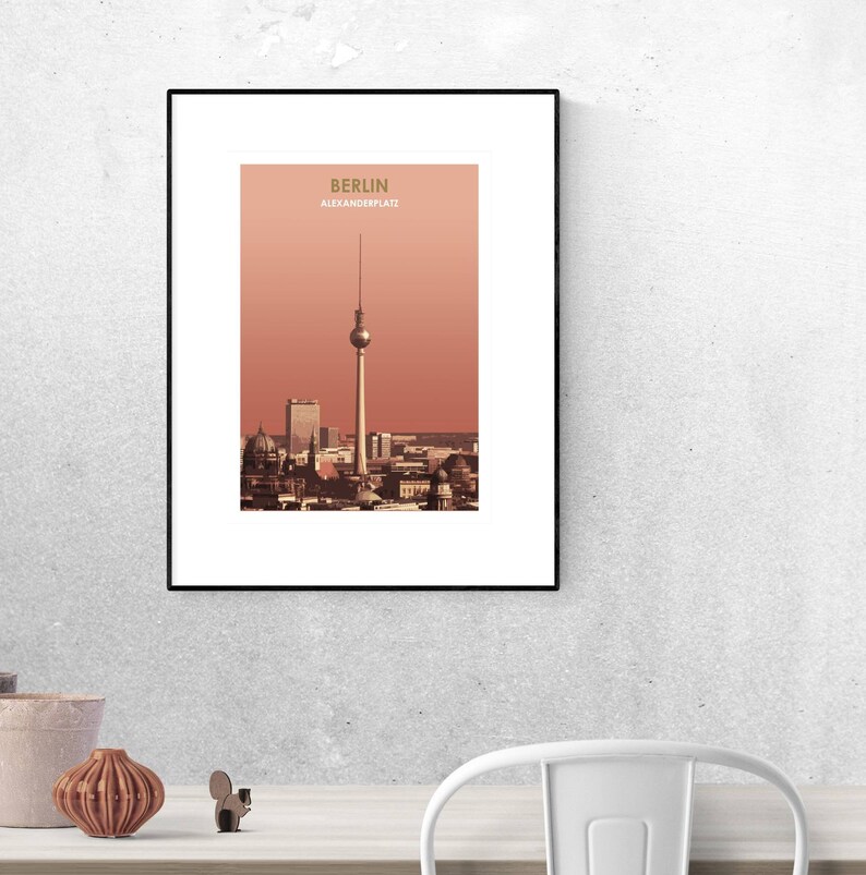 May include: A framed print of a cityscape with a tall tower in the center. The print is titled "Berlin Alexanderplatz" and has a red-orange background.