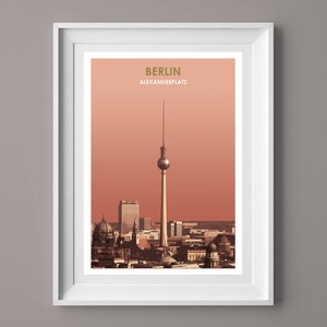 May include: A framed print of a cityscape with the Berlin Television Tower in the center. The print has a peach background and the text "BERLIN ALEXANDERPLATZ" in gold lettering.