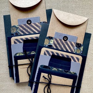 May include: Two sets of stationery, each with a kraft paper envelope, dark blue cardstock, and various patterned cards. The sets are tied with black twine. The cards feature stripes and vintage-style designs.