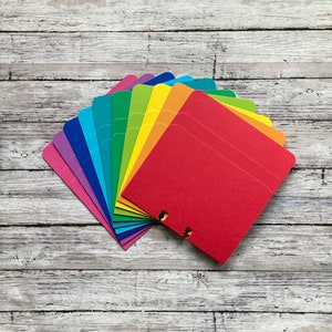 May include: A rainbow fan of colorful paper cards, with each card a different shade of the rainbow, from purple to red. The cards are stacked and fanned out, creating a rainbow effect.