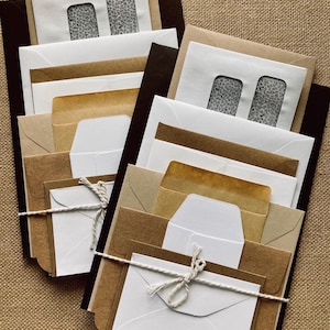 May include: A collection of assorted envelopes in various sizes and colors, including white, brown, and black. Some envelopes have window cutouts, and others are tied with twine. The envelopes are arranged in stacks.