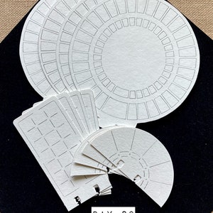 May include: A set of white paper planner templates with different designs, including circles, squares, and semi-circles. The templates are on a black surface and have the text "DAY 83" printed on them.