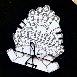 May include: A black and white illustration of a craft supply box with paintbrushes, paint tubes, and jars tied with twine.