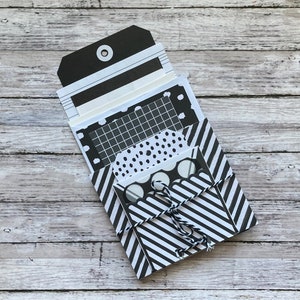 May include: A set of black and white patterned paper cards, folded and tied together with twine. The cards are arranged in a stack, with the top card featuring a black and white striped pattern.