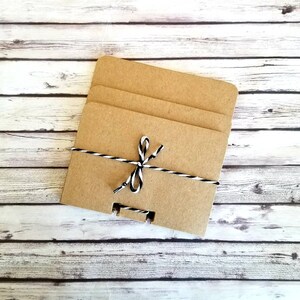 May include: Three brown cardboard squares stacked on top of each other, tied together with a black and white twine bow.
