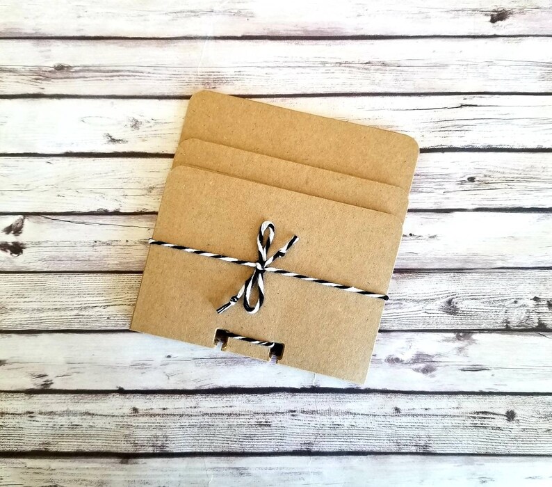 May include: Three brown cardboard squares stacked on top of each other, tied together with a black and white twine bow.