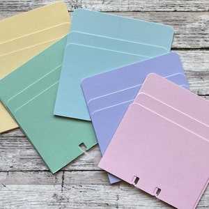 May include: A set of four stacks of colorful cardstock paper in yellow, green, blue, and purple. Each stack has three sheets of paper.