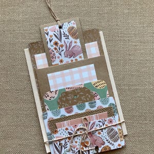 May include: A set of six Easter-themed gift tags with bunny and egg designs. The tags are made of brown cardstock and feature a variety of patterns, including floral, polka dot, and gingham. The tags are tied together with twine.