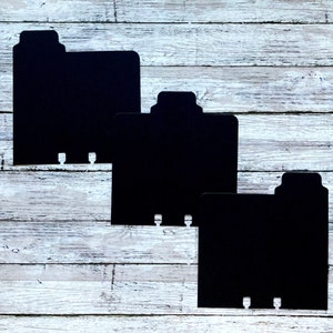 May include: Three black cardboard folder dividers with tabs on the top edge. The dividers are arranged in a descending size order, with the largest divider at the top and the smallest divider at the bottom.