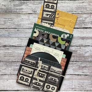 May include: A stack of paper goods with a vintage music theme. The top sheet features a black and white pattern of cassette tapes. The second sheet is a green sheet with the words "Universal Adventurer Vinyl Records". The third sheet is a black and white pattern of triangles. The bottom sheet is a brown woodgrain pattern.