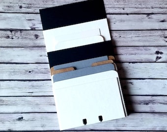 May include: A set of six blank cards with black, white, gray, and brown paper. The cards are stacked on top of each other and have a hole punched in the top corner.