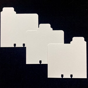 May include: Four white card dividers with tabs. The dividers are arranged in a row, with the largest divider on the left and the smallest divider on the right.