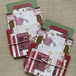 May include: Two bundles of handmade paper ephemera. Each bundle includes red, green, and cream-colored tags and cards with floral and script designs. The word "documented" is printed on a small card in each bundle. Bundles are tied with twine.