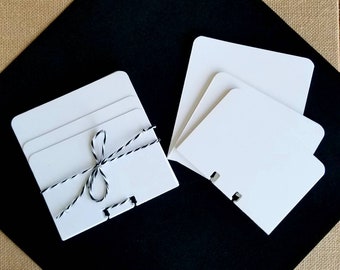May include: A set of three white cardstock notecards with a black and white twine bow. The notecards are folded in half and have a small hole punched in the top corner.