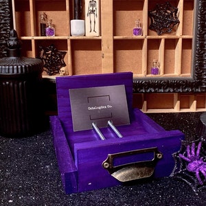 May include: A purple wooden drawer with a metal handle and two metal rods. The drawer is open and has a card inside that says "Catalogdex Co."