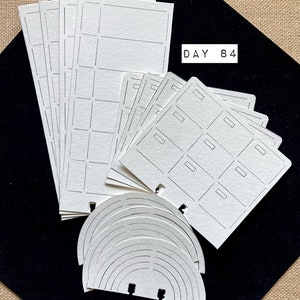 May include: A set of printable planner stickers with a grid pattern, a rainbow design, and a section with six boxes. The text "DAY 84" is printed on one of the stickers.