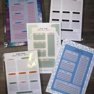 Peut inclure: Plusieurs blocs-notes Brain Dump avec des designs variés. Les blocs-notes comportent des sections pour les listes de tâches, les pensées et les notes. Les couleurs incluent le rose pastel, le bleu, le vert et le blanc, avec des bordures à motifs. Le texte "Brain Dump Make Some Space" est visible.
