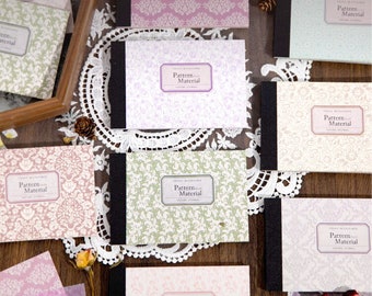 May include: A collection of small, patterned notebooks with the text "Pattern Material" on the cover. The notebooks are arranged on a lace doily and a wooden surface.