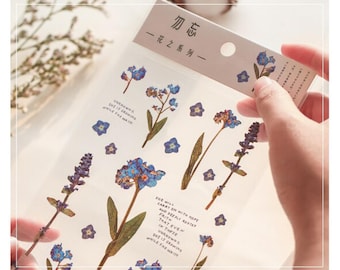 May include: A sheet of clear stickers with pressed forget-me-not flowers and lavender. The stickers are on a white background with the text "勿忘 一花之系列一" in black.