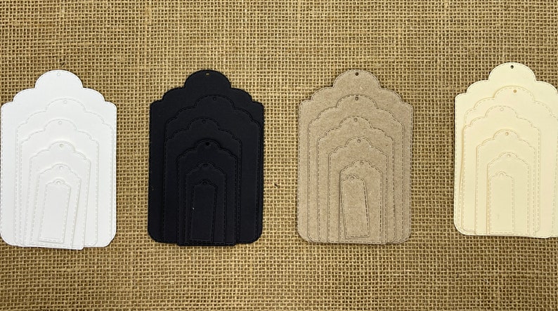 May include: Set of five nested, scalloped-edge gift tags in white, black, beige, and cream. The tags are made of cardstock and have a hole at the top for string or ribbon.