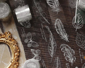 May include: Assortment of clear washi tape rolls with white designs of butterflies, feathers, and leaves. The text "Romantic field" is printed on the tape.