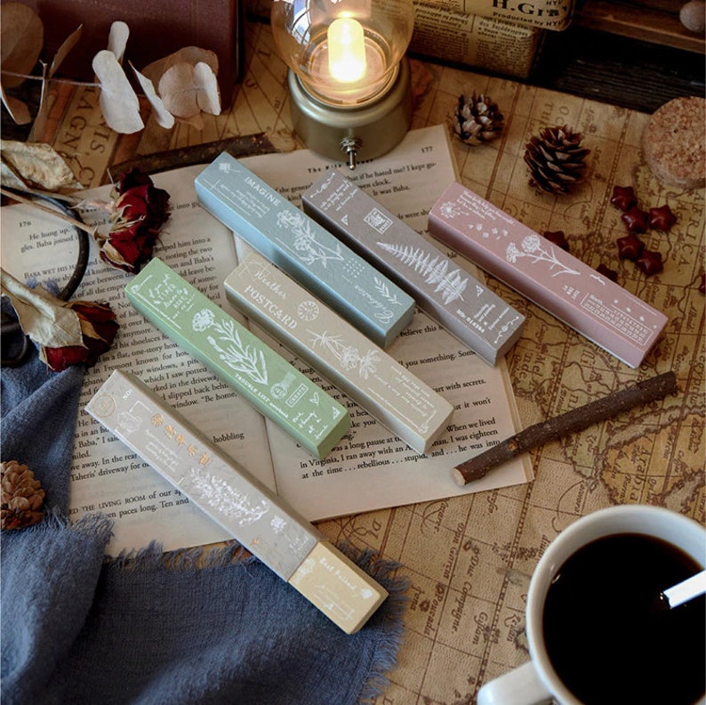 May include: Set of six wooden stamps with floral designs. The stamps are rectangular and have a light wood finish. The stamps are labelled with the words "Imagine", "Weather Postcard", "Africa", "No", "Tip", and "Mel".