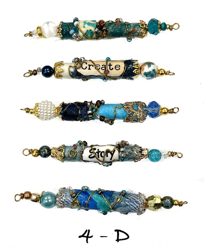 May include: Five blue and white beaded jewelry pieces with gold wire accents. The beads are wrapped with fabric and have words on them, including "Create" and "Story".