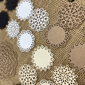 May include: Assortment of white, cream, and brown paper doilies with intricate lace designs. The doilies are arranged on a burlap background.