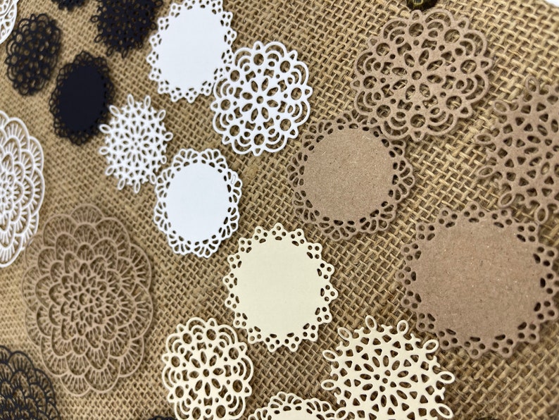 May include: Assortment of white, cream, and brown paper doilies with intricate lace designs. The doilies are arranged on a burlap background.