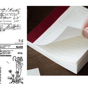 Może przedstawiać: Mały, czerwony, liniowany notes z białą okładką. Notes jest otwarty i widoczne są jego strony. Na okładce znajduje się czarno-biała pieczątka z napisem "Montre Lumineuse "LE ROYAL" 22 4th."