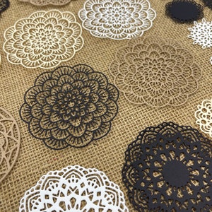 May include: Assortment of paper doilies in various sizes and colors, including white, black, and brown. The doilies have intricate lace patterns and are arranged on a burlap background.