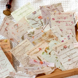 Puede incluir: Una colecci&oacute;n de ef&iacute;meras de papel de estilo vintage con dise&ntilde;os florales y texto escrito a mano. El papel es beige y marr&oacute;n con una superficie texturizada. El texto incluye frases como "Escucha a tu coraz&oacute;n", "Cree", y "Ronda y ronda".