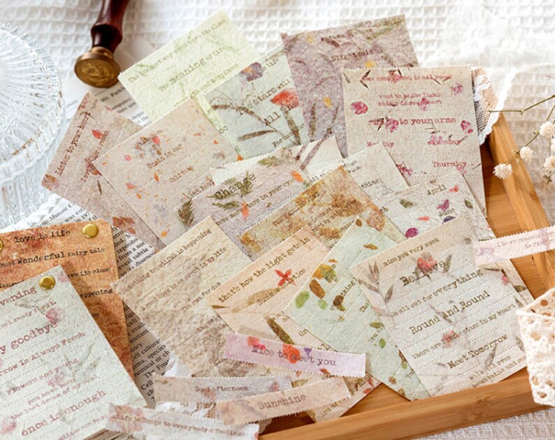 Puede incluir: Una colecci&oacute;n de ef&iacute;meras de papel de estilo vintage con dise&ntilde;os florales y texto escrito a mano. El papel es beige y marr&oacute;n con una superficie texturizada. El texto incluye frases como "Escucha a tu coraz&oacute;n", "Cree", y "Ronda y ronda".