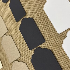 May include: Assortment of blank gift tags in various colors and materials, including white, black, and brown. The tags have a scalloped edge and a hole for string or ribbon.