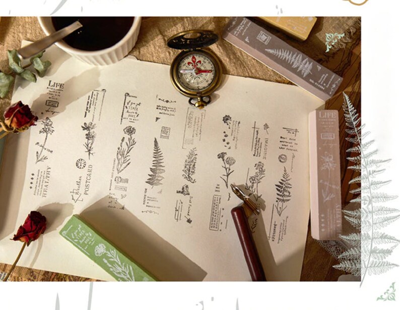 May include: A set of 10 clear rubber stamps featuring floral and fern designs. The stamps are arranged on a white paper background with a compass, a pen, and other stamps. The stamps include words such as "Life", "Imagine", "Healthy", and "Postcard".