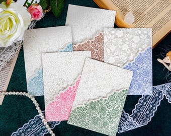 May include: Six white cards with intricate lace patterns, each with a different colored inner layer. The colors are blue, pink, green, brown, and two white cards.