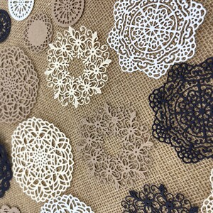May include: Assortment of white, black, and brown paper doilies with intricate lace designs. The doilies are arranged on a burlap background.