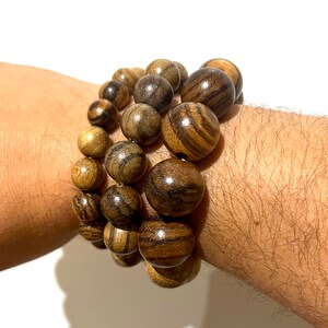 May include: A set of three bracelets made of dark brown wood beads. The beads are round and have a natural wood grain pattern.