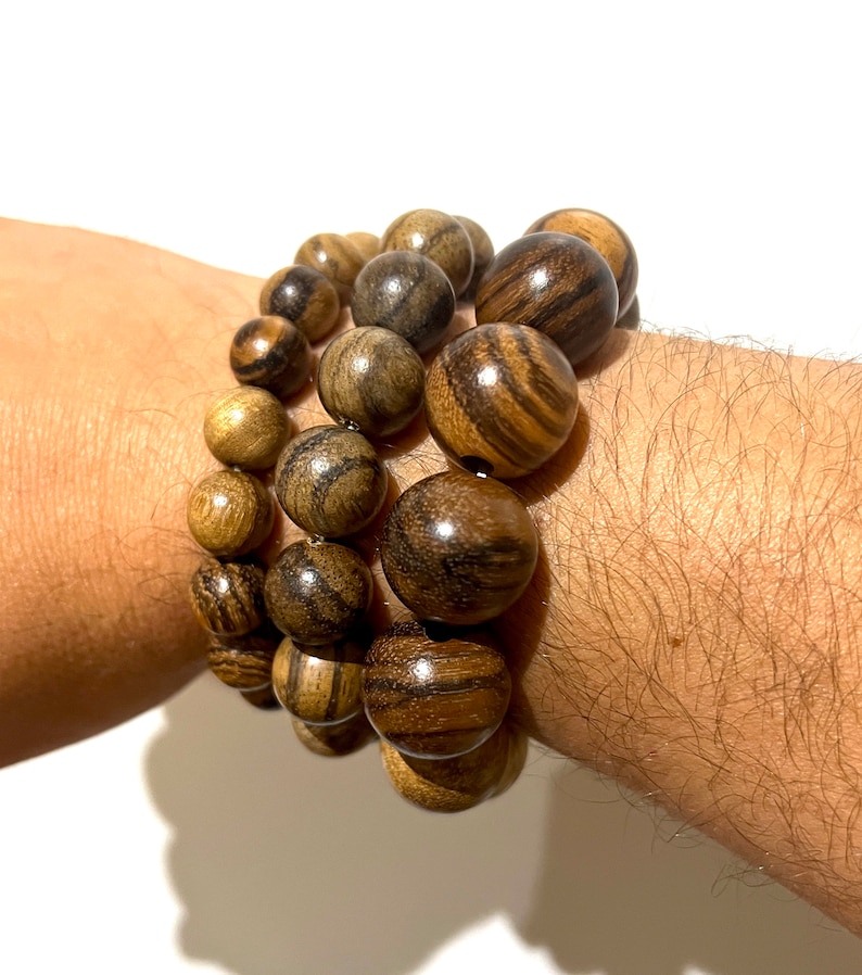 May include: A set of three bracelets made of dark brown wood beads. The beads are round and have a natural wood grain pattern.