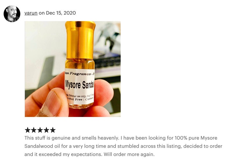 Op de afbeelding: Een klein, doorzichtig glazen flesje met een gouden dop en een etiket met de tekst "Mysore Sandal" en "Alcohol Free". Het flesje wordt vastgehouden door een hand.